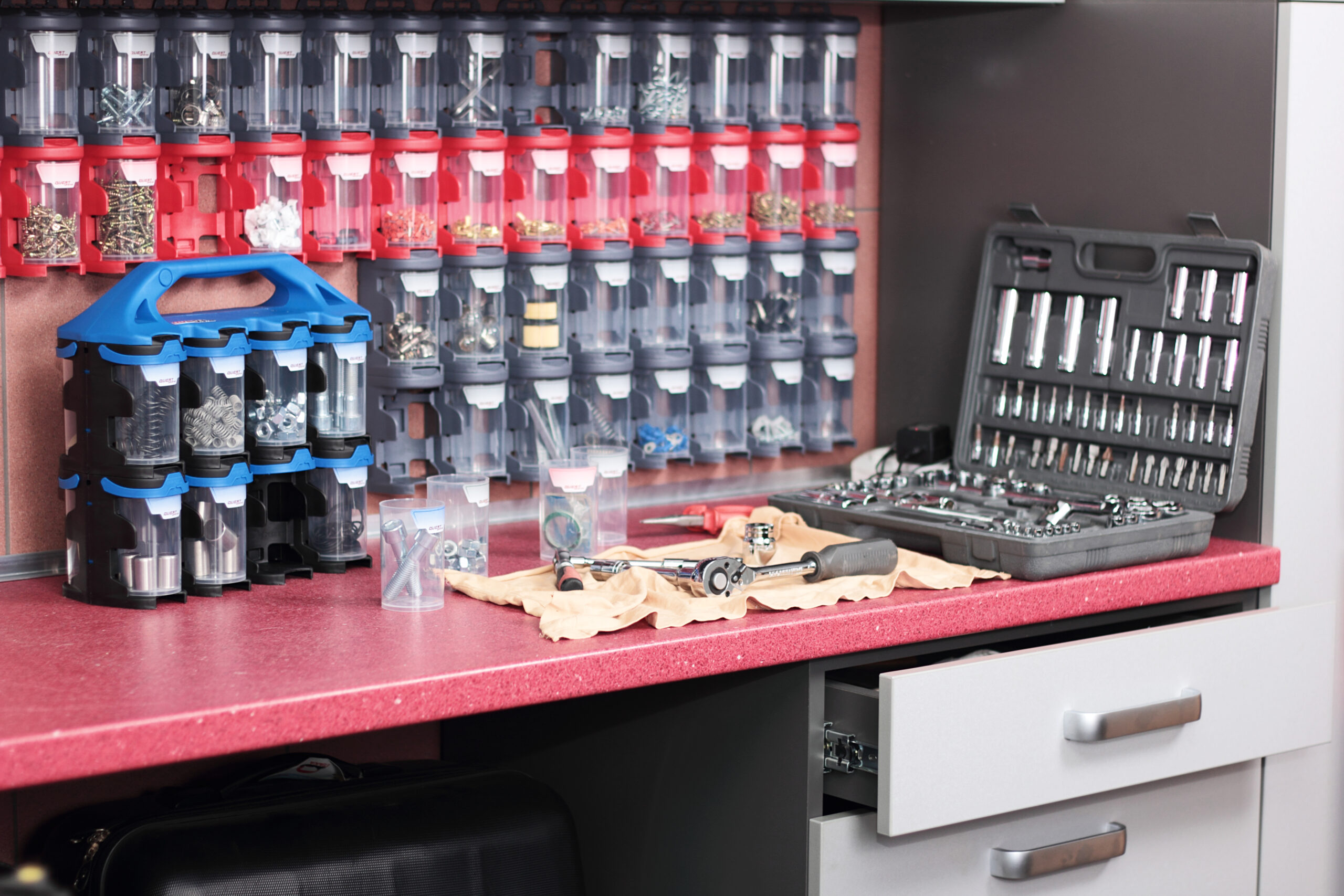 Zorganizowana ściana w warsztacie z narzędziami oraz czerwonymi pojemnikami modułowymi Quest System do przechowywania drobnych elementów.